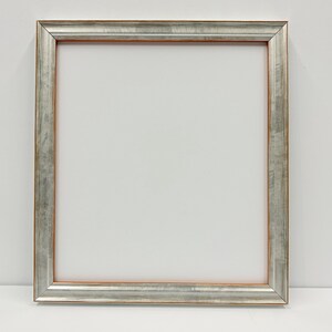 May include: A rectangular picture frame featuring a metallic silver finish with visible brushstroke textures. The inner edge of the frame displays a thin, warm copper-colored border, providing a distinct contrast against the silver surface.