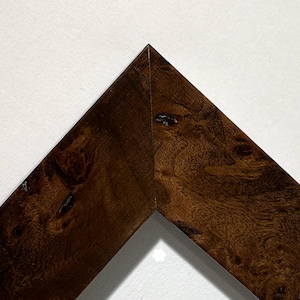 May include: Close-up of a corner of a wooden picture frame. The frame is a rich, dark brown with a visible wood grain pattern. The corner is precisely joined, showcasing the craftsmanship of the frame.