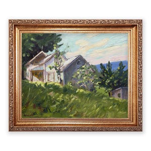 May include: Oil painting of a rural landscape featuring a white house with a gray roof, surrounded by green trees and tall grass. The artwork is framed in a gold-colored, ornate frame, adding a touch of elegance to the pastoral scene.