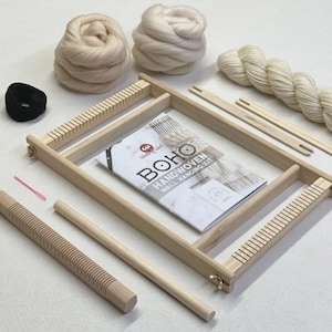 May include: A complete kit for making a Boho handwoven wall hanging. The kit includes a wooden frame, yarn, wool roving, a comb, and a needle. The kit also includes a booklet with instructions. The colours are neutral, with light beige and natural wood tones.