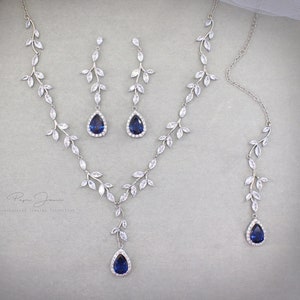 May include: A silver necklace and earrings set with a blue teardrop-shaped stone and a leaf design. The jewelry is made of silver and cubic zirconia.