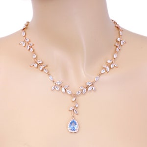 May include: A rose gold necklace with a delicate leaf design and a teardrop-shaped blue gemstone pendant.