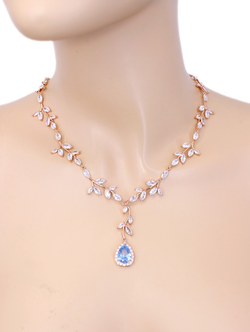 May include: A rose gold necklace with a delicate leaf design and a teardrop-shaped blue gemstone pendant.