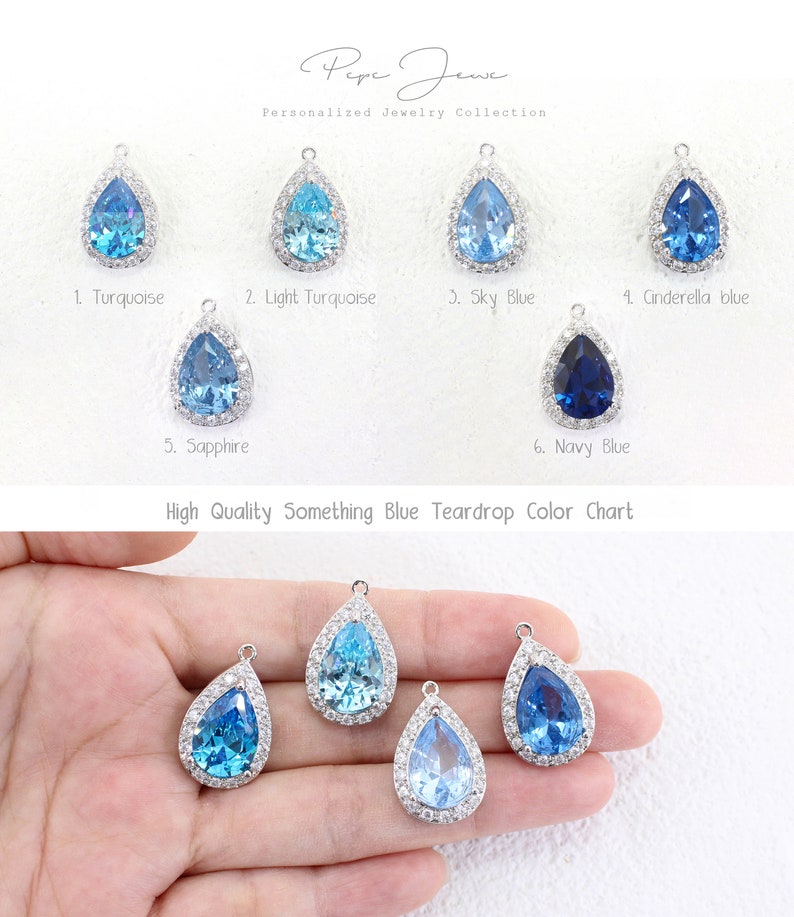 May include: Color chart of teardrop-shaped crystal pendants in various shades of blue, including turquoise, light turquoise, sky blue, sapphire, and navy blue. The pendants are set in silver and have a halo of small clear crystals around the center stone. The text "High Quality Something Blue Teardrop Color Chart" is printed below the pendants.