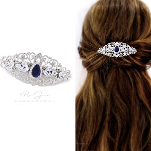 Puede incluir: Un peine de pelo plateado con una piedra azul en forma de l&aacute;grima rodeada de diamantes de imitaci&oacute;n transparentes. El peine est&aacute; decorado con un delicado dise&ntilde;o de filigrana.