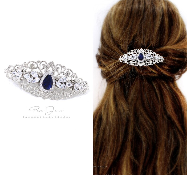 Puede incluir: Un peine de pelo plateado con una piedra azul en forma de l&aacute;grima rodeada de diamantes de imitaci&oacute;n transparentes. El peine est&aacute; decorado con un delicado dise&ntilde;o de filigrana.