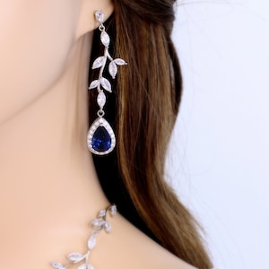 May include: A pair of silver earrings with a blue teardrop-shaped stone and a leaf design. The earrings are dangling and have a delicate look.