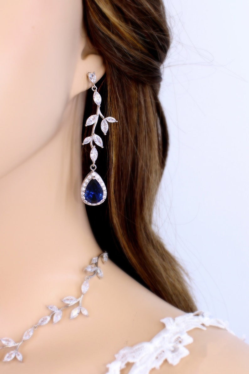 May include: A pair of silver earrings with a blue teardrop-shaped stone and a leaf design. The earrings are dangling and have a delicate look.