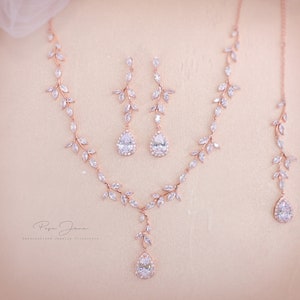 May include: A rose gold bridal jewelry set with a delicate leaf design and pear-shaped crystal accents. The set includes a necklace, earrings, and a bracelet.
