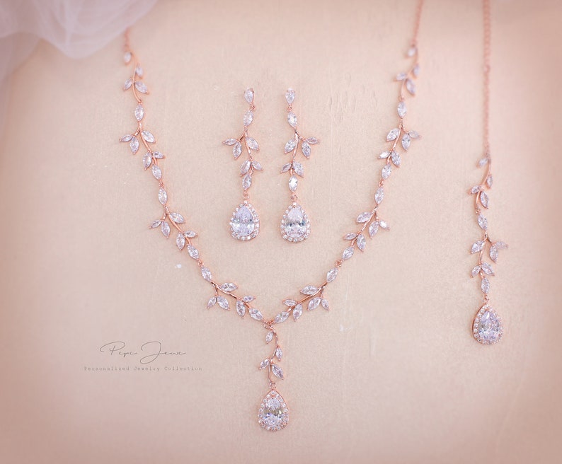May include: A rose gold bridal jewelry set with a delicate leaf design and pear-shaped crystal accents. The set includes a necklace, earrings, and a bracelet.