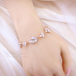 Puede incluir: Un brazalete de oro rosa con un dise&ntilde;o delicado que presenta piedras de circonita c&uacute;bica transparentes dispuestas en forma de hoja. El brazalete se muestra en la mu&ntilde;eca de una modelo.