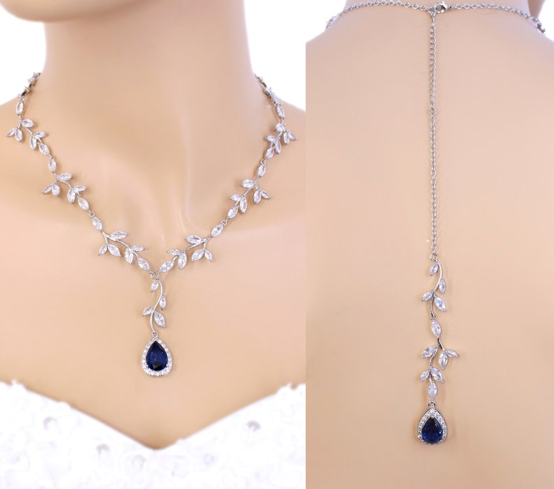 May include: A silver necklace with a teardrop-shaped blue gemstone pendant and a matching back necklace. The necklace features a delicate leaf design with clear crystals.