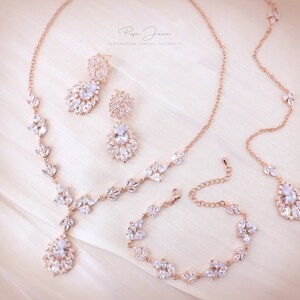 Puede incluir: Conjunto de joyas de novia de oro rosa con collar, pendientes y pulsera. Las joyas presentan un delicado dise&ntilde;o de hojas con piedras transparentes brillantes.