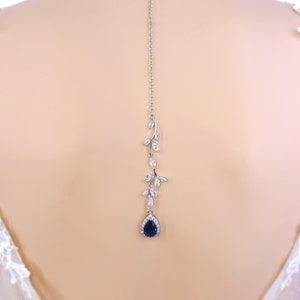 May include: A silver back necklace with a teardrop shaped blue stone and a vine design with clear stones.