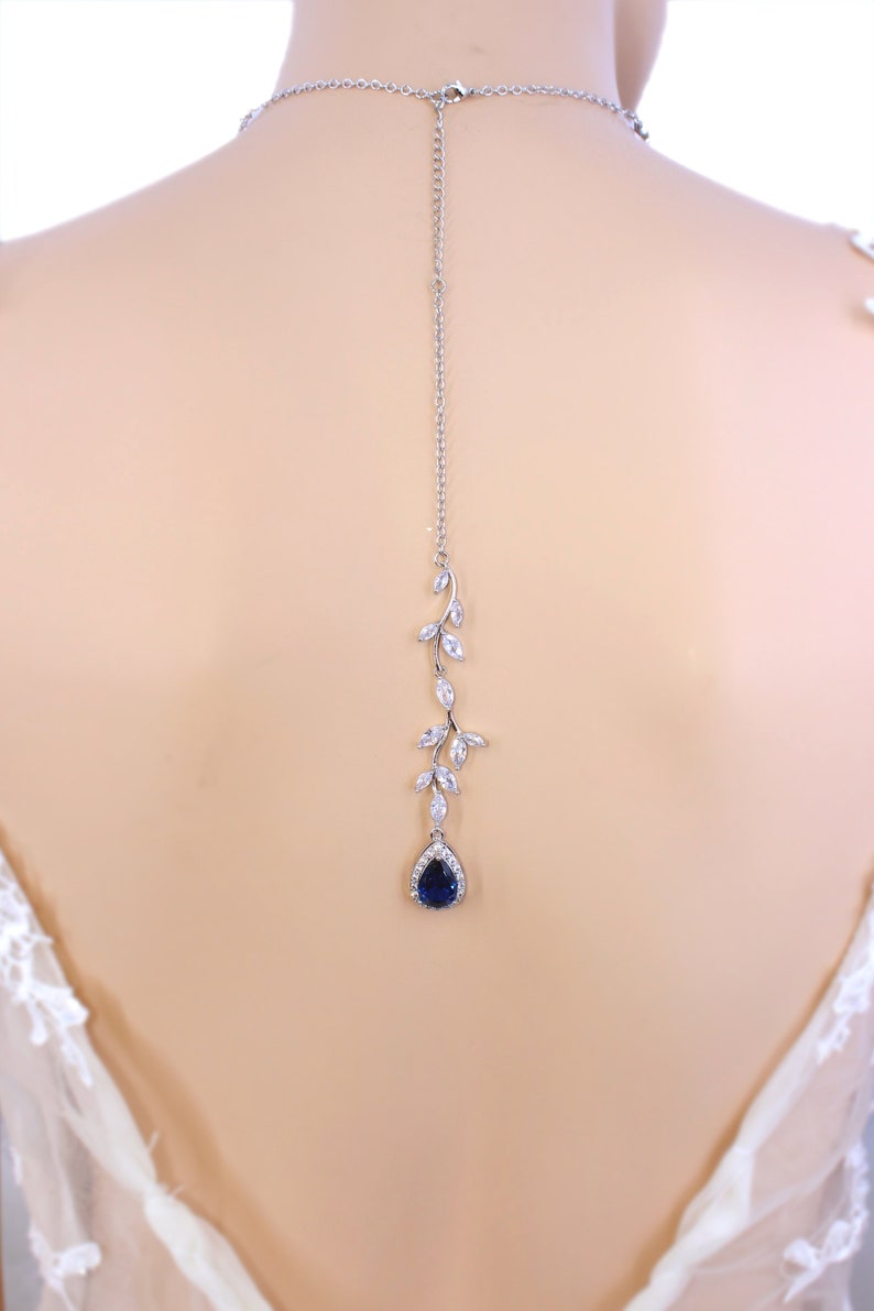 May include: A silver back necklace with a teardrop shaped blue stone and a vine design with clear stones.