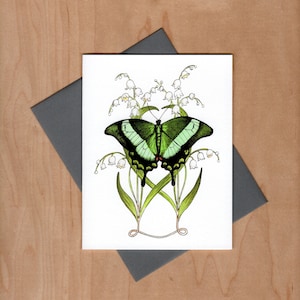 Watercolor pen and ink illustrated note card.  Emerald green peacock butterfly sits in front of Lilly-of-the-valley flowers