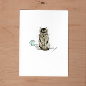 Front of greeting card;  pen and watercolor illustration of a long haired cat sitting in the middle of an open book a pen and cup sit to the side