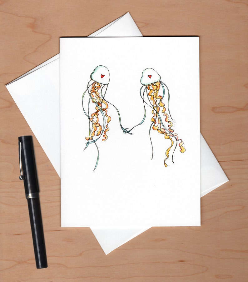 Peut inclure: Une carte blanche avec une illustration dessin&eacute;e &agrave; la main de deux m&eacute;duses avec des c&oelig;urs rouges sur la t&ecirc;te. Les m&eacute;duses se tiennent la main et ont de longues tentacules flottantes.