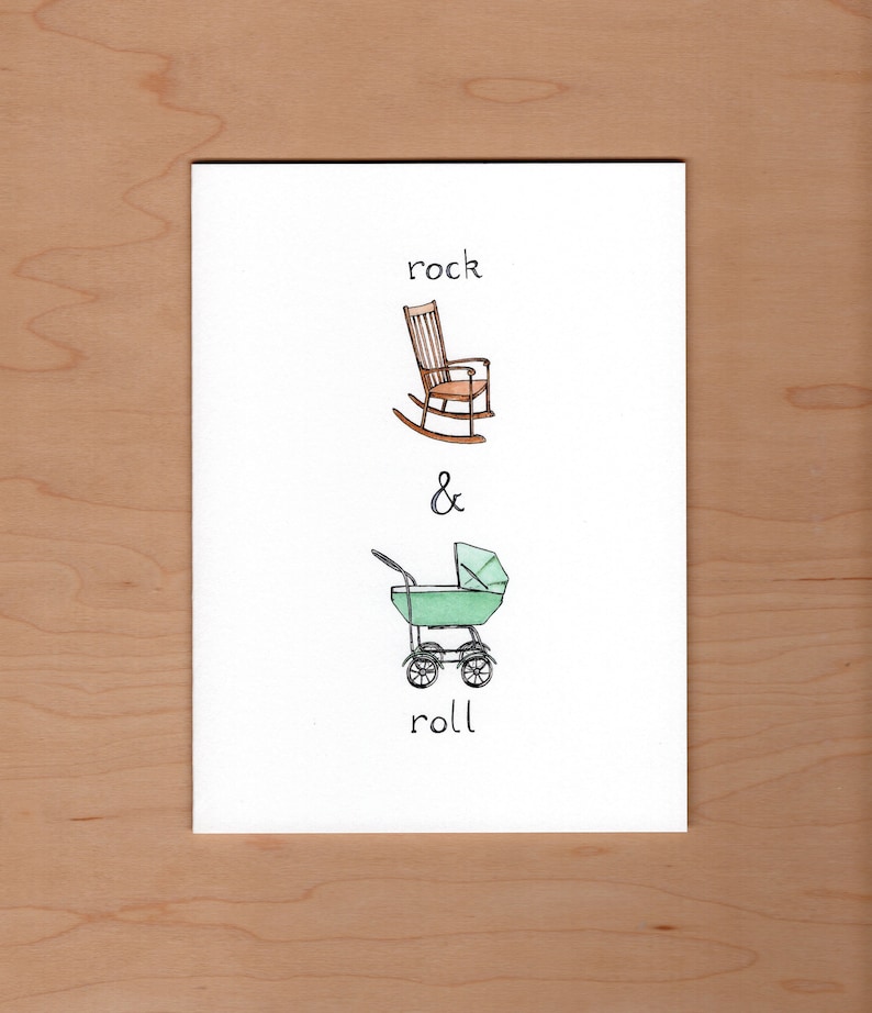 May include: A white card with a hand-drawn illustration of a rocking chair and a baby stroller. The text "rock & roll" is written below the illustration.