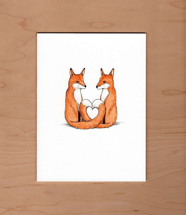 front of card; pen and watercolor illustration of two red foxes sit facing each other their tails curl and touch forming a heart