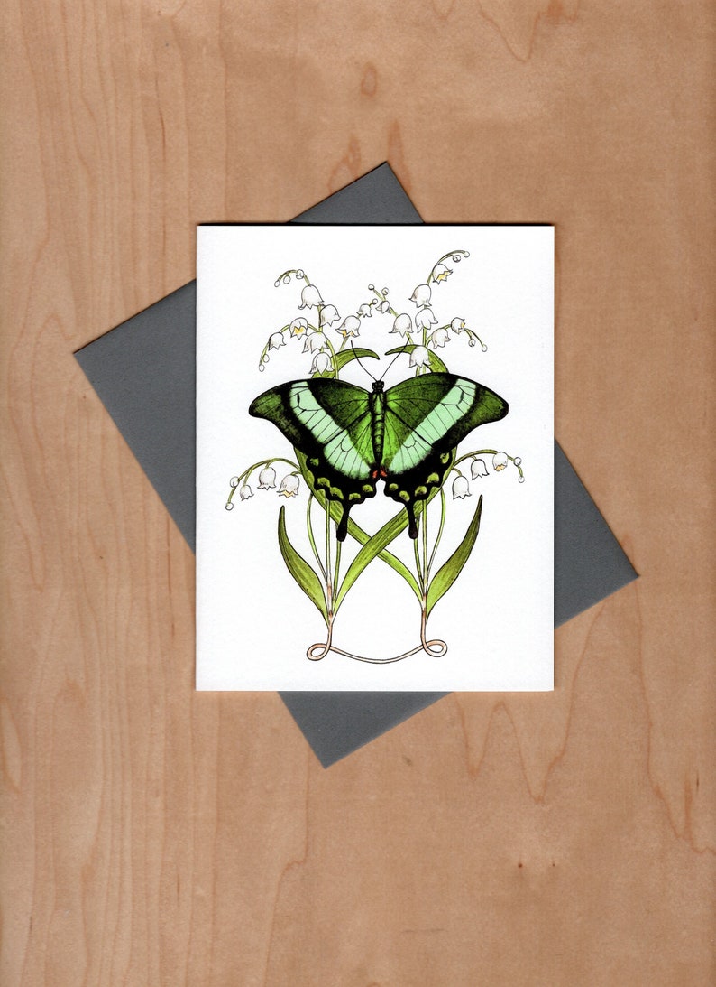 Watercolor pen and ink illustrated note card.  Emerald green peacock butterfly sits in front of Lilly-of-the-valley flowers