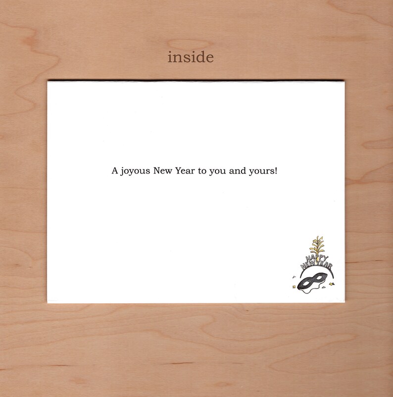 Peut inclure: Une carte blanche avec le texte "inside" en haut et le texte "A joyous New Year to you and yours!" au milieu. Une illustration en noir et blanc d'un masque avec une couronne dor&eacute;e et des confettis en bas.