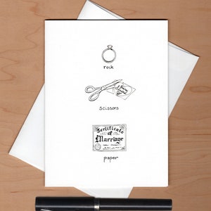 May include: A white card with a black and white illustration of a ring, scissors cutting a heart-shaped piece of paper with the text "You're Engaged", and a certificate of marriage. The text "rock", "scissors", and "paper" is written below each illustration.