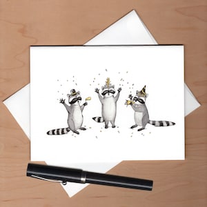 Peut inclure: Trois ratons laveurs portant des chapeaux de f&ecirc;te et tenant des cadeaux de f&ecirc;te. Les ratons laveurs sont debout en rang et sont entour&eacute;s de confettis. L'arri&egrave;re-plan est blanc.