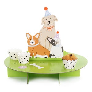 May include: A green, tiered cardboard display featuring illustrations of three dogs wearing party hats. The display includes two cupcake holders with black polka dots, a bone, and a cupcake. The dogs are a golden retriever, a corgi, and a French bulldog.