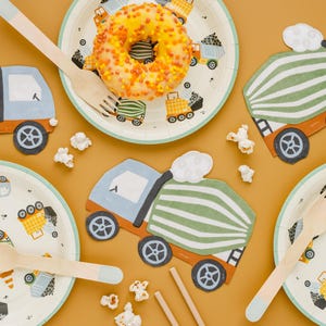 May include: A festive party scene with construction-themed decorations. Includes paper plates and truck-shaped cutouts, wooden forks, and a glazed donut. The plates feature colorful construction vehicles. Popcorn is scattered around the scene.