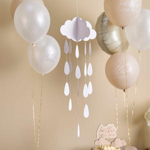 Puede incluir: Decoración de baby shower con globos blancos y beige, un móvil de nube y gotas de lluvia, y una pequeña tarta con un letrero de "hello little one". Los globos son de varias formas y tamaños, algunos impresos con la misma frase.