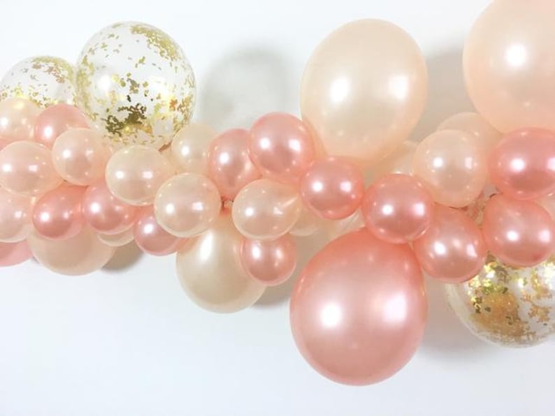 May include: A garland of peach and ivory balloons with gold confetti. The balloons are arranged in a cascading pattern.
