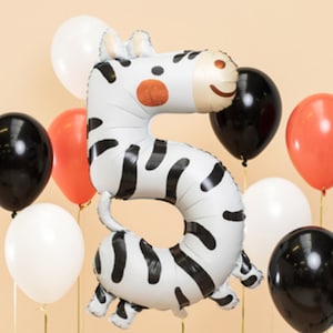 May include: A collection of balloons, including a large number 5 shaped balloon designed as a zebra. The balloons are white, black, and coral, perfect for a birthday celebration. The zebra balloon has a smiling face.