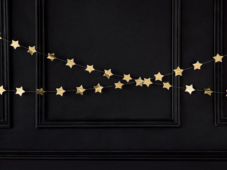 May include: A gold star garland with a black background. The garland is made of paper stars strung together with a thin string.