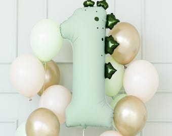 May include: A light green number one balloon surrounded by pastel-colored balloons in shades of white, gold, and light green. The number one balloon has dark green accents and is likely for a first birthday celebration.