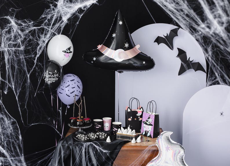 May include: A Halloween party table setting with black and purple balloons, a black witch hat balloon, and black bats. There are also black and white gift bags with Halloween characters, black and white cups, and black and white candy on a black tablecloth.