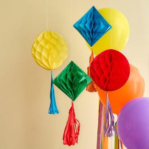 Pode incluir: Uma disposição festiva de decorações suspensas e balões em várias cores. Inclui bolas de favo de mel amarelas, decorações de papel em forma de diamante azul e verde e balões vermelhos, laranja e roxo, criando um ambiente festivo.