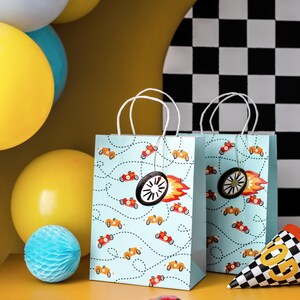 K&ouml;nnte beinhalten: Zwei hellblaue Geschenkt&uuml;ten mit wei&szlig;en Griffen sind mit orangefarbenen und roten Rennwagen und gepunkteten Linien verziert. Jede Tasche hat einen schwarzen Radanh&auml;nger mit einer roten und orangefarbenen Flamme. Gelbe und blaue Luftballons sind im Hintergrund.
