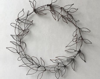 May include: A decorative wreath made from dark brown wire, shaped into a circular form. The wire is crafted into leaf shapes and woven together. This handcrafted wreath is suitable for interior decoration.