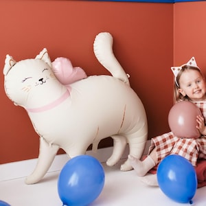 May include: A white cat-shaped foil balloon with pink wings and a girl wearing a star-shaped headband and a red and white checkered dress holding a pink balloon.