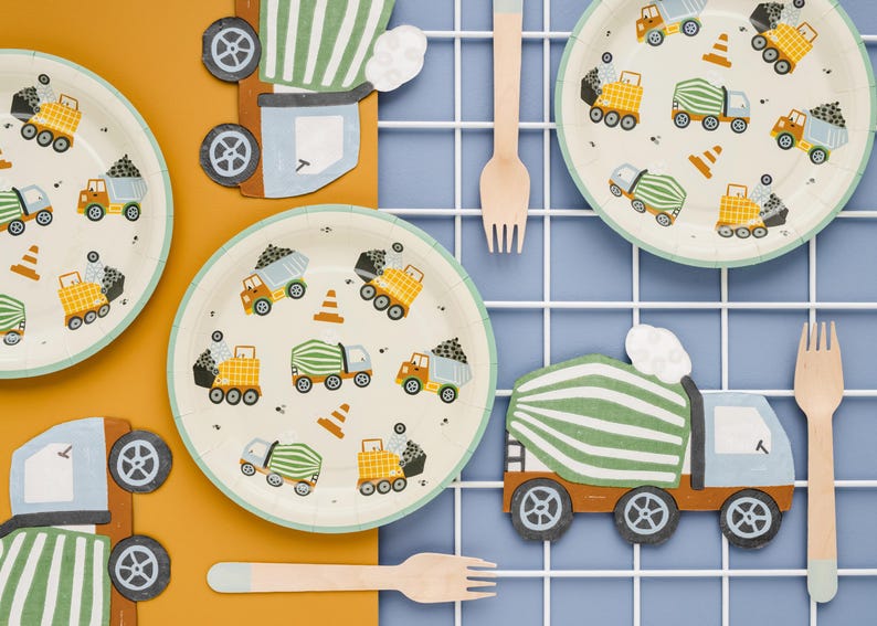 May include: Construction-themed party supplies, including plates, forks, and truck-shaped decorations. The plates feature illustrations of dump trucks, cement mixers, and traffic cones. The color palette includes beige, orange, green, and blue.