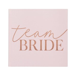 Op de afbeelding: Een roze vierkant notitieboekje met de tekst "Team Bride" in ros&eacute;goud.