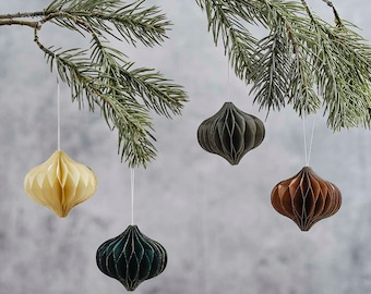 May include: Three paper Christmas ornaments hanging from a pine branch. The ornaments are in the shape of a teardrop and are made of folded paper. The ornaments are green, brown, and cream.