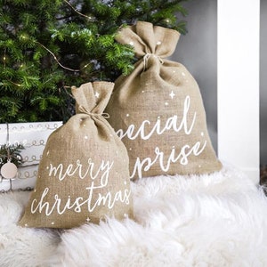 May include: Two burlap gift bags with white lettering. One bag says "merry christmas" and the other says "special surprise".