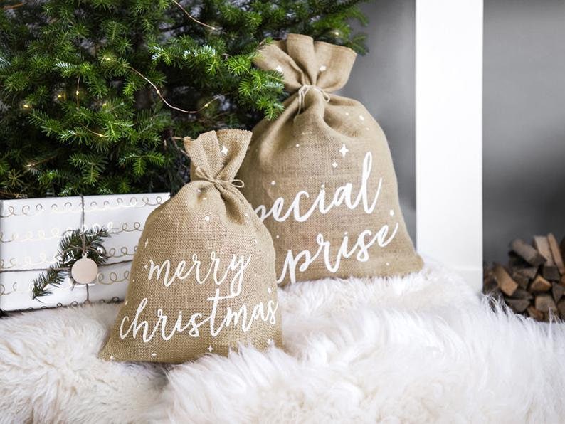 May include: Two burlap gift bags with white lettering. One bag says "merry christmas" and the other says "special surprise".