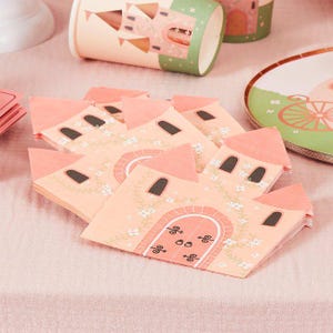 May include: A stack of paper napkins shaped like a castle with a peach-coloured facade, a central arched doorway, and dark windows. The design features white floral vines climbing the walls and pointed roof sections in a matching peach tone.