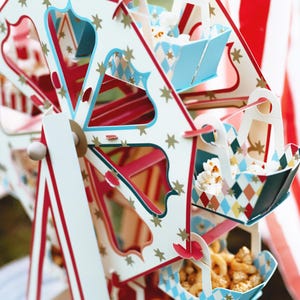 May include: A white, red, and blue cardboard Ferris wheel with a star pattern. Each car of the Ferris wheel holds a different snack, including popcorn, pretzels, and other treats.