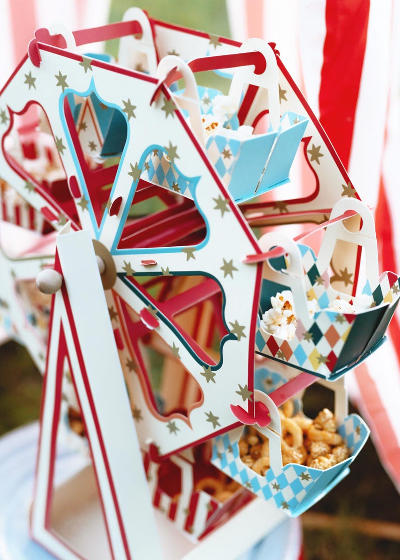 May include: A white, red, and blue cardboard Ferris wheel with a star pattern. Each car of the Ferris wheel holds a different snack, including popcorn, pretzels, and other treats.