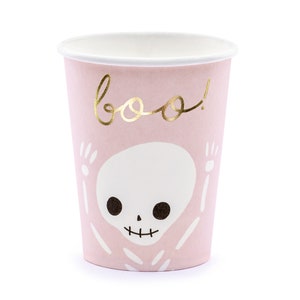 May include: A pink paper cup with a white interior and a gold "boo!" script. The cup features a white skeleton design with black eyes and a smiling mouth, perfect for Halloween parties.