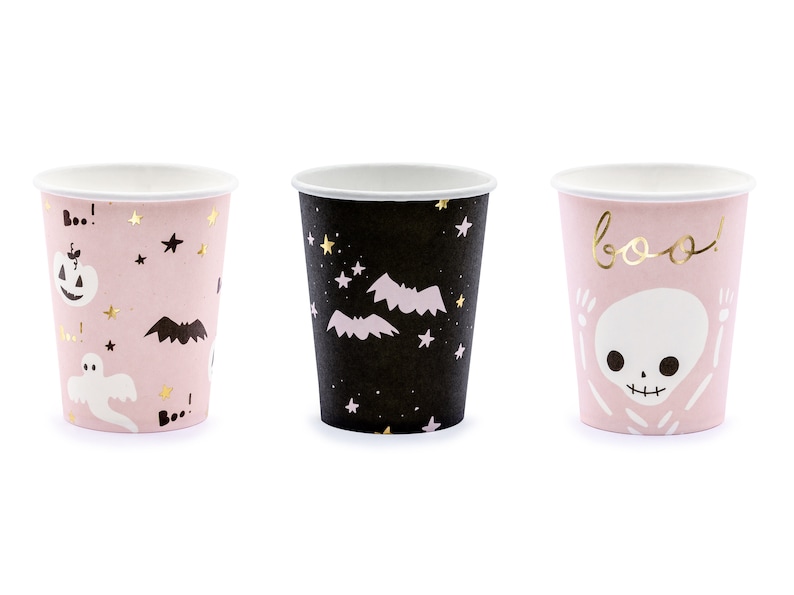 May include: Three paper cups with Halloween-themed designs. One cup is black with bats and stars, another is pink with a ghost, pumpkin, and stars, and the third is pink with a skeleton and the word "boo!"